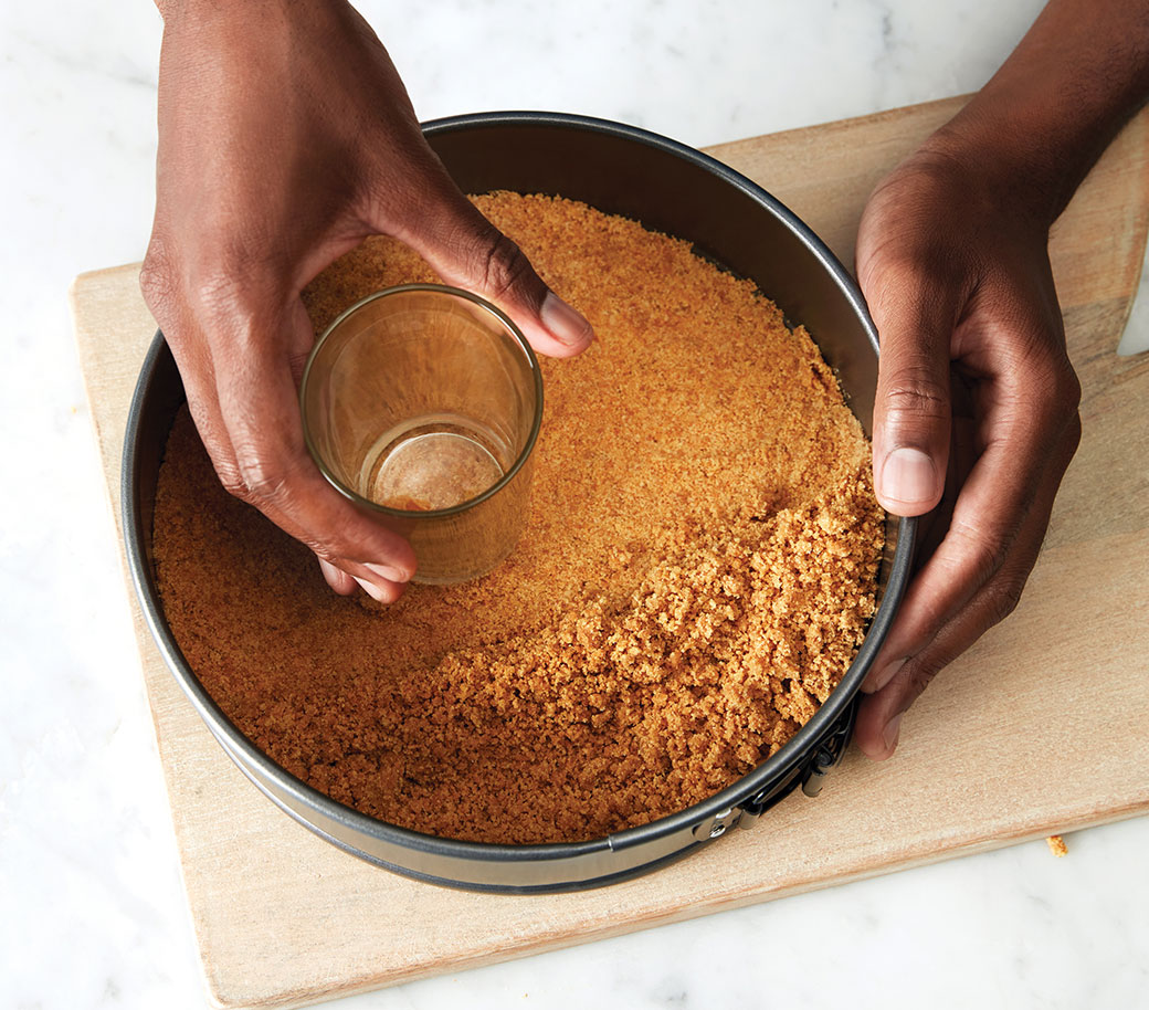 image of hands pressing crumbs into pan using a glass