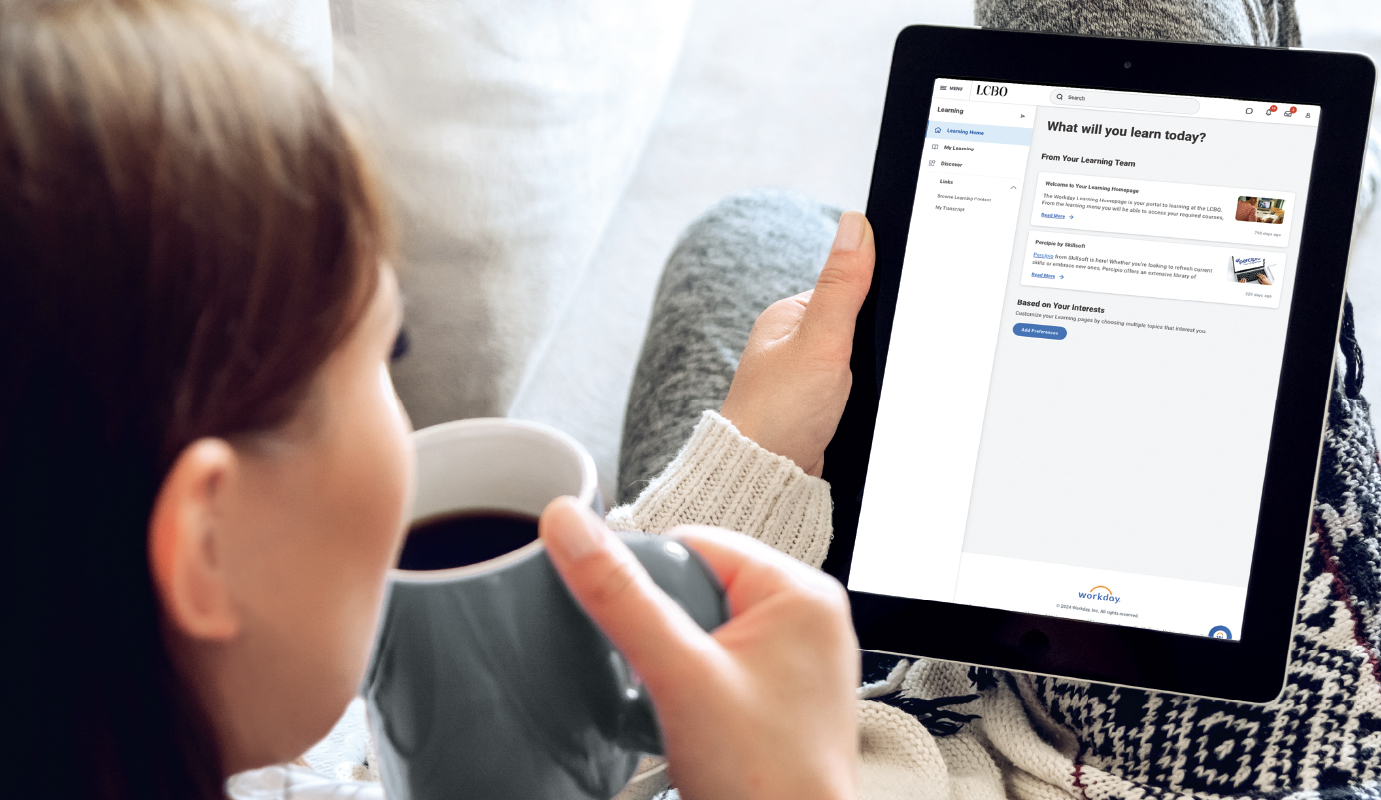 Une femme participe à une formation pour les employés sur sa tablette tout en dégustant un café, ce qui témoigne d’un environnement de travail productif et détendu.