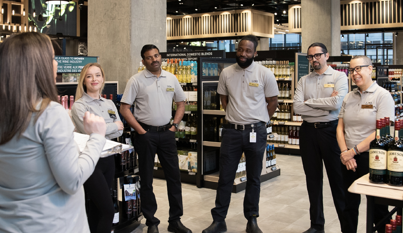 Groupe d’employés apprenant les uns des autres en cercle dans une succursale de la LCBO, favorisant le travail d’équipe et le partage des connaissances.