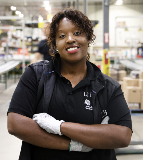 Une employée d’entrepôt de la LCBO au sourire éclatant, portant des gants de travail blancs, debout dans un entrepôt de la LCBO.